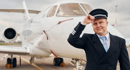 Posing for a camera. Experienced pilot in uniform standing outside near plane.